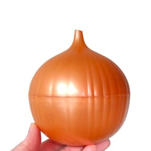 May include: A brown, onion-shaped container with a ridged surface. The container is held in a hand against a white background. The container is made of plastic and has a small stem at the top.