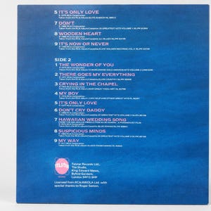 The back of a blue cardboard record sleeve displaying a printed tracklist and a pink circular logo against a white background.