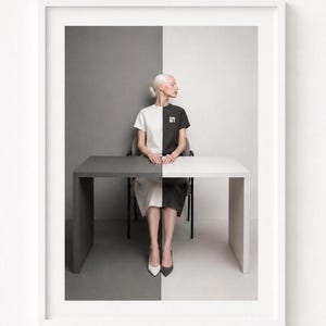 White framed minimalist photographic wall art mockup on a clean white wall featuring a woman seated at a split black-and-white table against a monochrome background. Contemporary modern printable art with geometric composition, neutral tones, and Scandinavian gallery style.