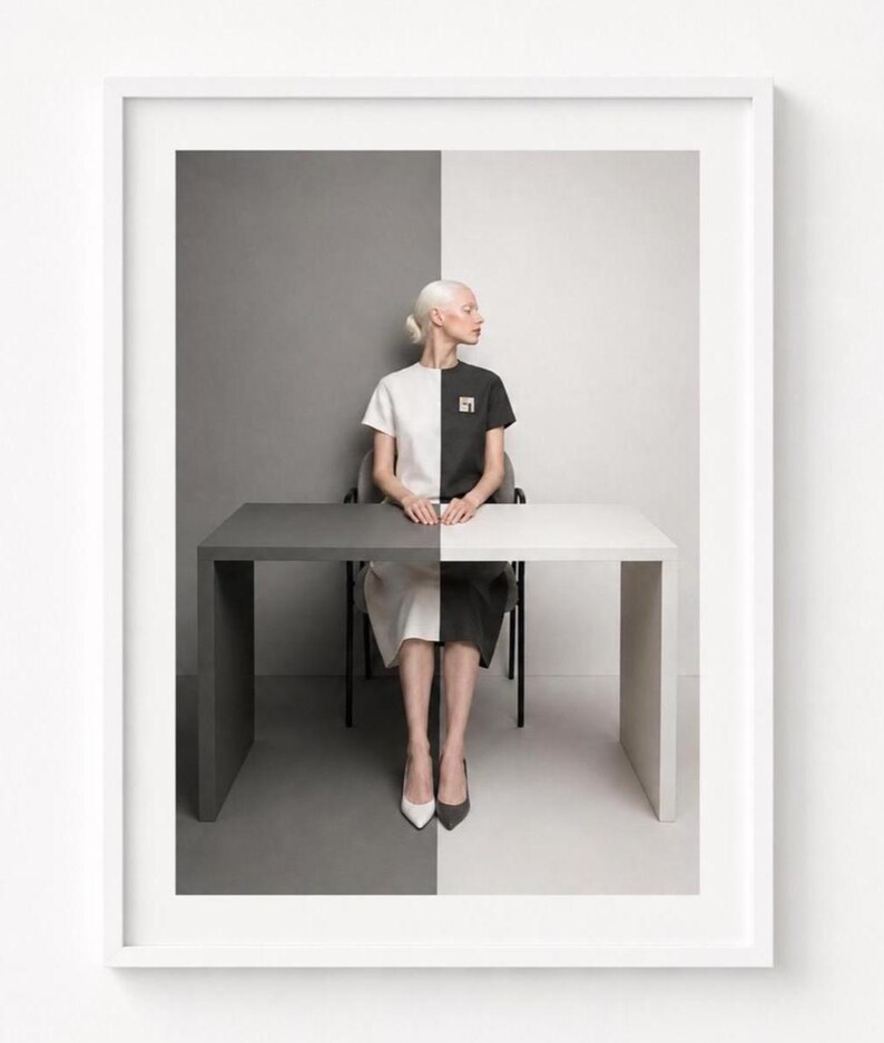 White framed minimalist photographic wall art mockup on a clean white wall featuring a woman seated at a split black-and-white table against a monochrome background. Contemporary modern printable art with geometric composition, neutral tones, and Scandinavian gallery style.