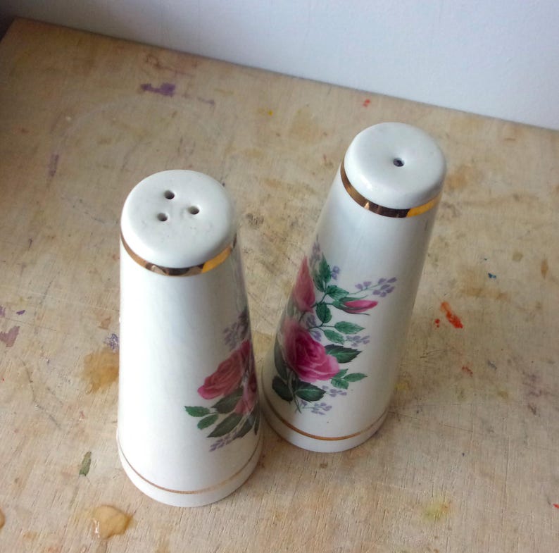 A pair of tall ceramic salt and pepper shakers with gold trim and rose transfers.