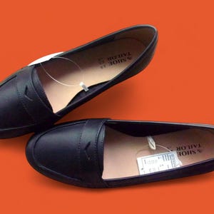 A pair of Vintage Loafers styled as Black Leather Loafers with a bow detail, these 1980s Leather Flats are timeless Bow Detail Loafers made from Soft Leather Shoes. Perfect as Retro Work Shoes, Minimalist Loafers, or Office Leather Flats, they channel Preppy Style Shoes and Quiet Luxury. Designed as Gender Neutral Shoes, they reflect Archive Fashion values and sustainable elegance in classic Leather Slip Ons.