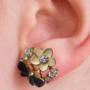 Close-up of vintage butterfly earrings featuring black white enamel wings and cz stud earrings set in gold plated studs. The enamel earrings have a cluster studs design with sculptural studs detailing, ideal for fans of retro earrings and statement studs. Lightweight and elegant, these dainty earrings are nature inspired, part of a slow fashion collection of handmade jewelry crafted for archival charm.