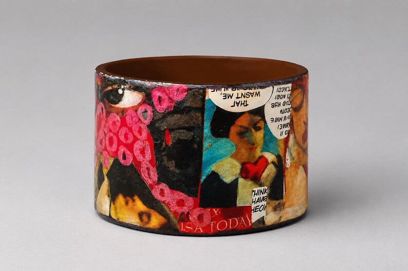 Handmade upcycled wood comic book bangle featuring a colourful Pop Art collage with speech bubbles, illustrated characters and bold red, black and turquoise details. Visible text includes “THAT WASN’T ME” and “USA TODAY.”