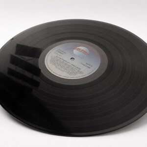 A black 12 inch vinyl record lies flat on a white surface with clear dark reflections across its grooved surface.