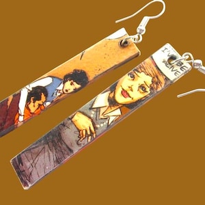 May include: A pair of long, rectangular earrings with a vintage comic book design. One earring features a woman with the text "I've Been Alive" and the other earring features a man and woman.