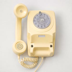 An overhead view of a cream-colored rotary dial telephone base station with the matching handset receiver resting vertically to its left side on a white background.