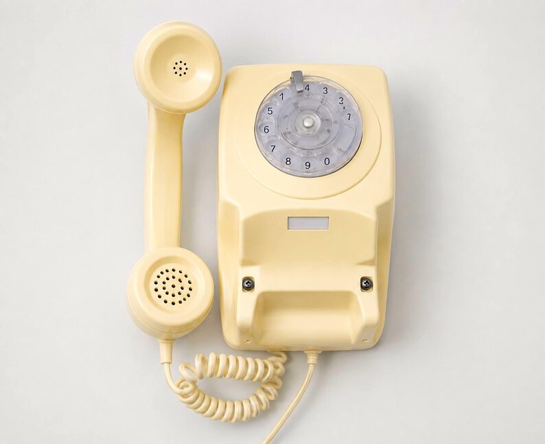 An overhead view of a cream-colored rotary dial telephone base station with the matching handset receiver resting vertically to its left side on a white background.