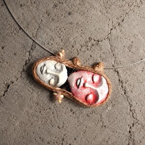 Two clay faces hand-shaped into an oval pendant bound by brown twine on a silver wire choker.