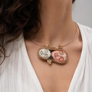 Two clay faces hand-shaped into an oval pendant bound by brown twine on a silver wire choker.