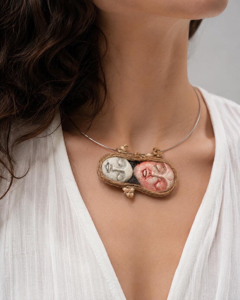 Two clay faces hand-shaped into an oval pendant bound by brown twine on a silver wire choker.