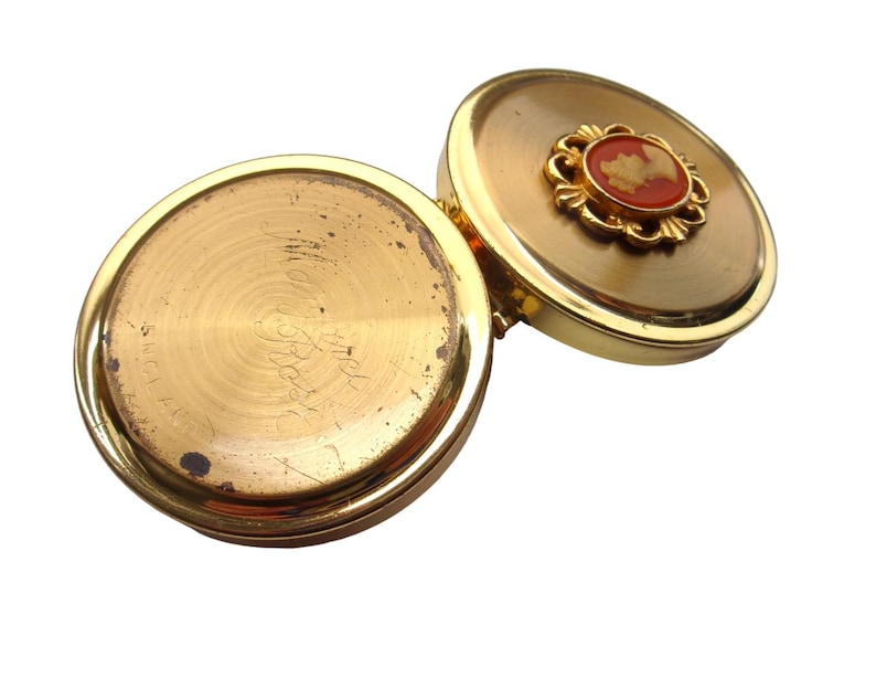 A small vintage pillbox with a red-and-ivory cameo trinket framed in gold filigree, this gold keepsake doubles as a mini treasure and handmade box. Styled as a regency charm, it’s perfect for gifting as a victorian gift or historical gift. The aged finish enhances its appeal as an antique case, ideal for retro cottage collectors seeking micro luxury and collectible art in a timeless rose gold box.