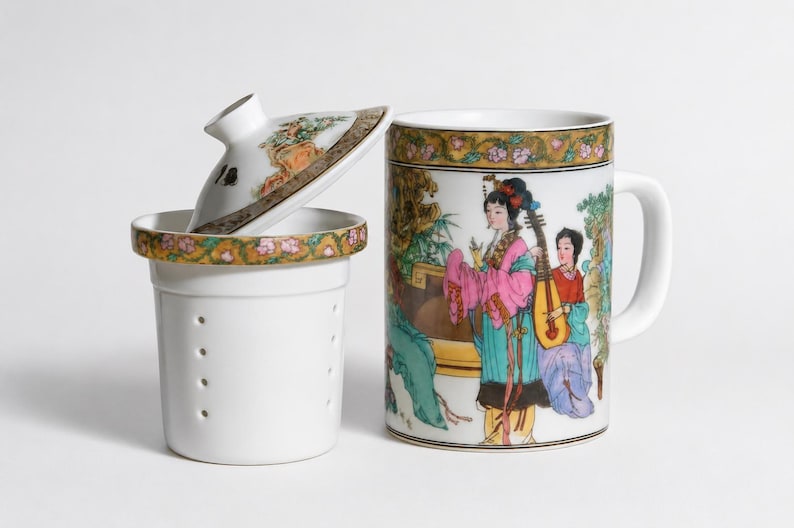 White porcelain three piece tea set including a straight sided mug with a handle decorated with a colorful illustration of asian women playing musical instruments in a garden a matching white ceramic infuser with drainage holes and a round white porcelain lid with floral borders on a plain white background.