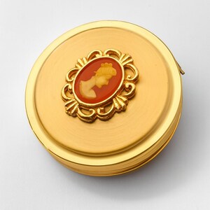 A small vintage pillbox with a red-and-ivory cameo trinket framed in gold filigree, this gold keepsake doubles as a mini treasure and handmade box. Styled as a regency charm, it’s perfect for gifting as a victorian gift or historical gift. The aged finish enhances its appeal as an antique case, ideal for retro cottage collectors seeking micro luxury and collectible art in a timeless rose gold box.