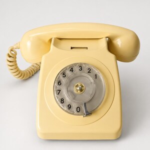 An overhead front view of a cream-colored rotary dial telephone with its handset resting horizontally across the cradle against a plain white background.