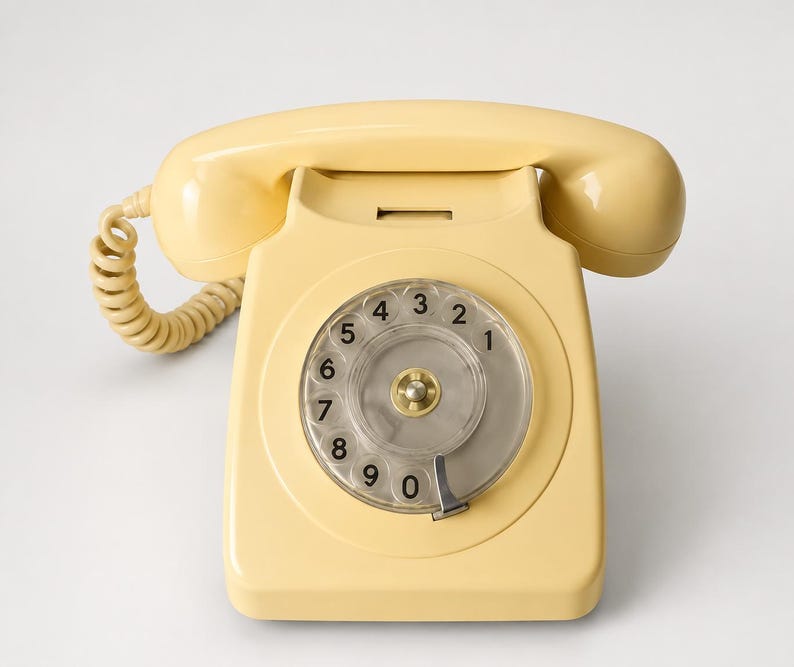 An overhead front view of a cream-colored rotary dial telephone with its handset resting horizontally across the cradle against a plain white background.