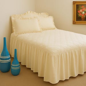 Peut inclure: Un lit crème avec une jupe de lit à volants et des oreillers assortis. Deux vases bleus à rayures blanches sont dans le coin. Une peinture florale encadrée est accrochée au mur, ajoutant une touche de couleur à la pièce.