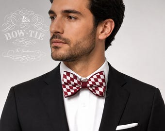 May include: A bow tie featuring a burgundy and white diamond checkered pattern. The bow tie is worn with a crisp white collared shirt and a black blazer. Text in the upper left corner reads The Tack London, Bow Tie, Pure Silk, For Gentlemen.