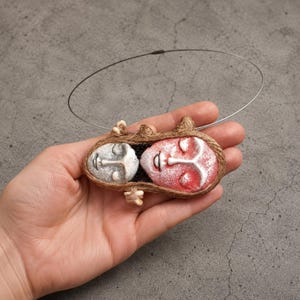 Two clay faces hand-shaped into an oval pendant bound by brown twine on a silver wire choker.