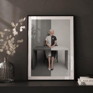 Minimalist black and white fashion photography print in a moody modern interior, framed wall art with subtle glass reflections, dark charcoal wall, smoked glass vase with dried white florals, contemporary Scandinavian home decor.