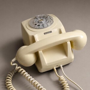 An overhead view of a cream-colored rotary dial telephone configured for wall mounting resting on a solid neutral gray surface.