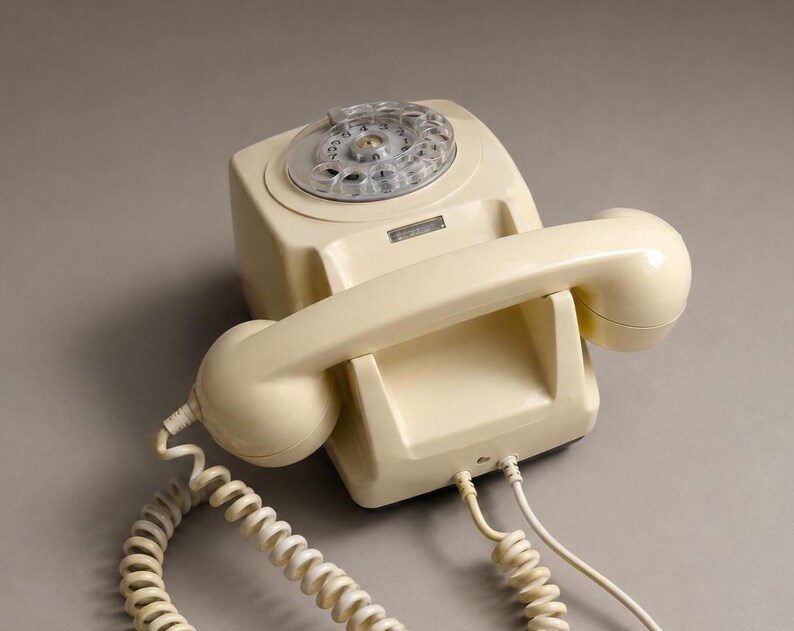An overhead view of a cream-colored rotary dial telephone configured for wall mounting resting on a solid neutral gray surface.