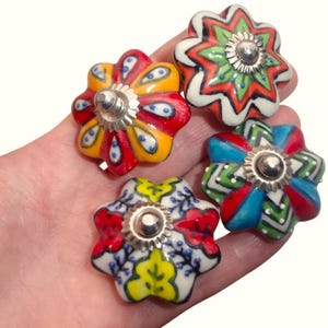 May include: Four colorful, flower-shaped ceramic cabinet knobs. Each knob features a unique design with vibrant colors like red, yellow, blue, and green, accented with silver-toned metal hardware. These decorative knobs add a touch of whimsy to any furniture piece.
