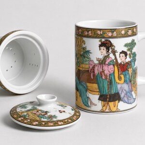 White porcelain three piece tea set including a straight sided mug with a handle decorated with a colorful illustration of asian women playing musical instruments in a garden a matching white ceramic infuser with drainage holes and a round white porcelain lid with floral borders on a plain white background.