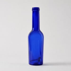 Vintage cobalt blue glass bottle with a tall narrow neck and rounded shoulders standing upright on a light grey-white studio background.