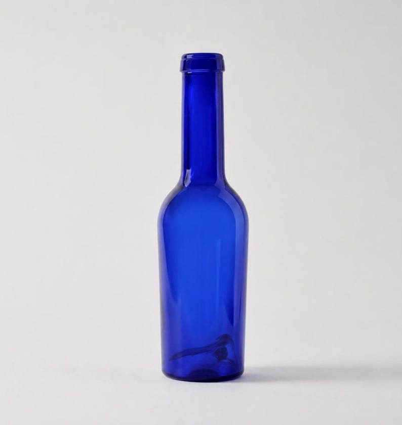 Vintage cobalt blue glass bottle with a tall narrow neck and rounded shoulders standing upright on a light grey-white studio background.