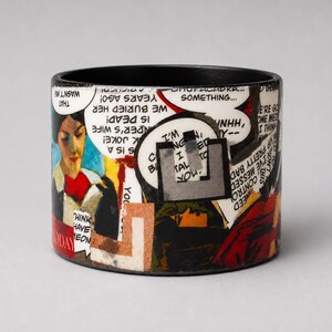Handmade Pop Art comic bangle featuring a bold collage of illustrated characters, speech bubbles, an eye motif and red graphic details. Visible comic text includes “WE BURIED HER,” “IS DEAD,” and “THAT WASN’T ME.”