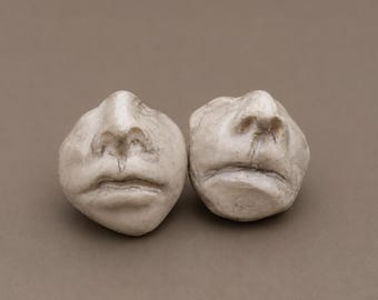 May include: Two off-white, textured sculptural objects shaped like human noses and mouths. These rounded, stone-like pieces feature detailed nostrils, philtrums, and lips with subtle grey shading in the crevices, creating a realistic, weathered appearance.