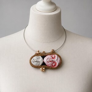 Two clay faces hand-shaped into an oval pendant bound by brown twine on a silver wire choker.