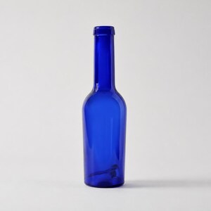 Tall vintage cobalt blue glass bottle with a slender neck and rounded shoulders, standing upright on a clean light grey-white studio background with a soft natural shadow.
