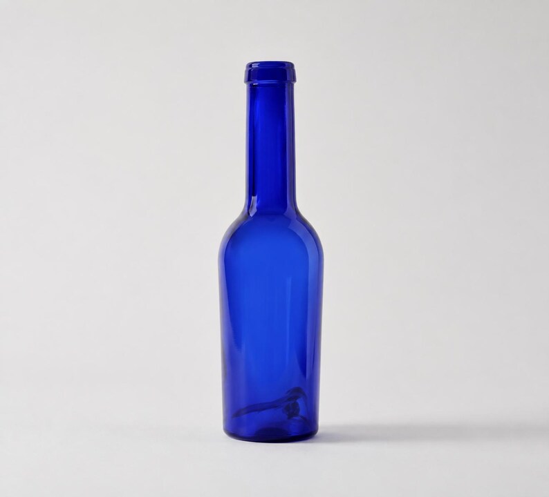 Tall vintage cobalt blue glass bottle with a slender neck and rounded shoulders, standing upright on a clean light grey-white studio background with a soft natural shadow.