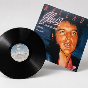 A black 12 inch vinyl record sits next to its illustrated Elvis Presley Ballads album cover on a white background.