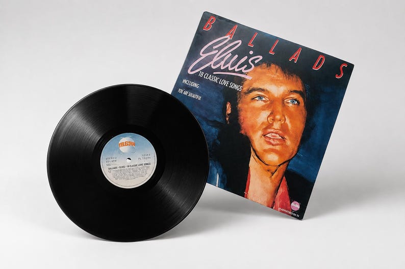 A black 12 inch vinyl record sits next to its illustrated Elvis Presley Ballads album cover on a white background.