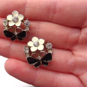 Close-up of vintage butterfly earrings featuring black white enamel wings and cz stud earrings set in gold plated studs. The enamel earrings have a cluster studs design with sculptural studs detailing, ideal for fans of retro earrings and statement studs. Lightweight and elegant, these dainty earrings are nature inspired, part of a slow fashion collection of handmade jewelry crafted for archival charm.