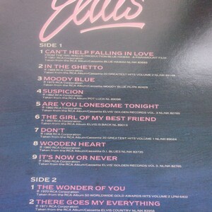 A close-up shot of the upper portion of a blue record sleeve back cover showing the tracklist text for Side 1 and Side 2 under a pink scripted Elvis logo.