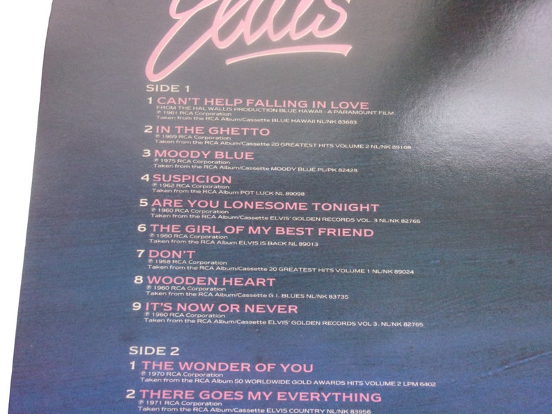 A close-up shot of the upper portion of a blue record sleeve back cover showing the tracklist text for Side 1 and Side 2 under a pink scripted Elvis logo.