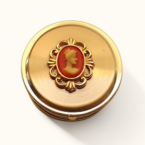 A small vintage pillbox with a red-and-ivory cameo trinket framed in gold filigree, this gold keepsake doubles as a mini treasure and handmade box. Styled as a regency charm, it’s perfect for gifting as a victorian gift or historical gift. The aged finish enhances its appeal as an antique case, ideal for retro cottage collectors seeking micro luxury and collectible art in a timeless rose gold box.