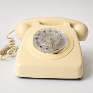 A front view of a cream-colored rotary dial telephone with the handset receiver resting on its cradle against a white background.
