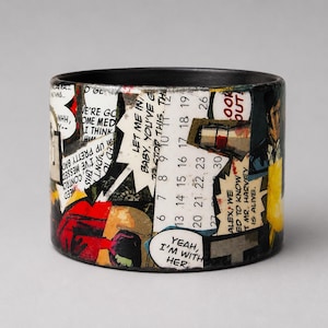 Handmade upcycled wood Comic Book bangle featuring a dramatic Pop Art collage with a large eye, pink circular graphics, illustrated figures and flames. Speech bubble reads “I...ADMIT, I WANTED YOU PUNISHED. I WAS ANGRY. B-BUT YOUR COMMANDING OFFICER... HE PUT ME IN MY PLACE.”