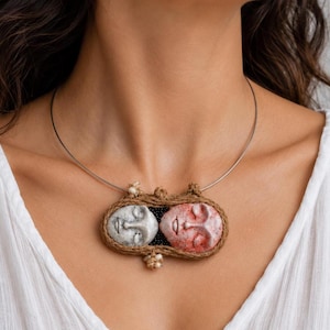 Two clay faces hand-shaped into an oval pendant bound by brown twine on a silver wire choker.