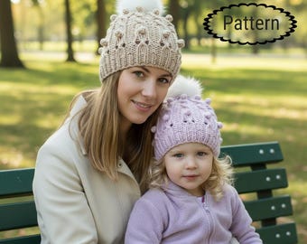 May include: Two knit beanies featuring a textured bobble pattern and a white pom-pom on top. One beanie is beige and the other is light purple. The word Pattern is printed in black text within a decorative oval frame in the upper right.
