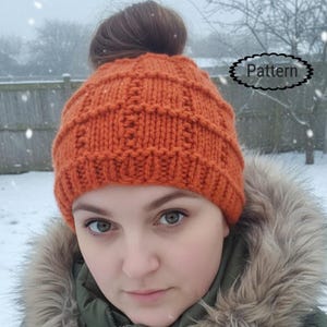 May include: An orange knitted beanie with a textured pattern. The hat is made of thick yarn and has a ribbed brim. The word "Pattern" is in a decorative oval. The beanie is worn in a snowy outdoor setting.