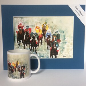 May include: A white ceramic mug with a colorful painting of horses and riders on a foggy racetrack. The mug is next to a framed painting of the same scene, with the artist's name "Rachel Ouston, Local Artist" in the top right corner.