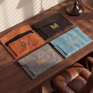 May include: Four rectangular document folders in tan, black, gray, and light blue. Each folder features a flap closure with a snap button and personalized gold or black lettering or symbols, including the names Morgan, Robert, and initials D|K and K.