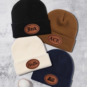Può includere: Quattro berretti di lana con nomi diversi su toppe di pelle. I berretti sono nero, marrone, bianco e blu navy. I nomi sulle toppe sono Jack, Ace, Halle e Bill.