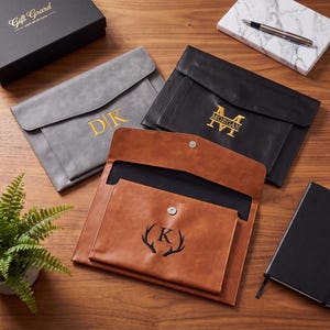May include: Three envelope-style document folders in grey, black, and tan leather-like material. The grey folder features gold monogram initials DK, the black folder has gold monogram MORGAN, and the tan folder has a black letter K with antlers.